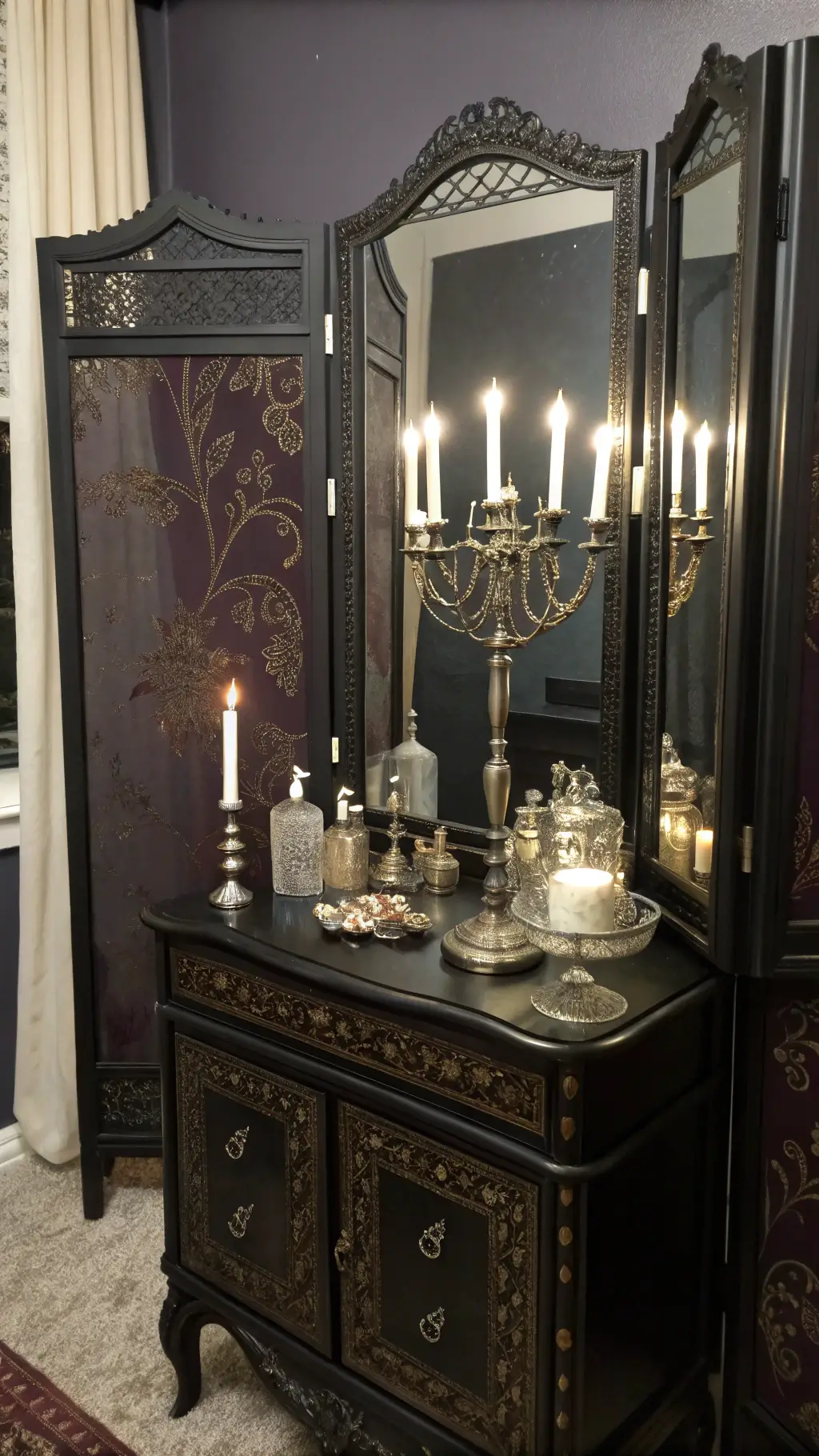 Dressing area with ornate black vanity, silver accessories, aubergine brocade screen, illuminated by candlelight reflected in a three-panel mirror.