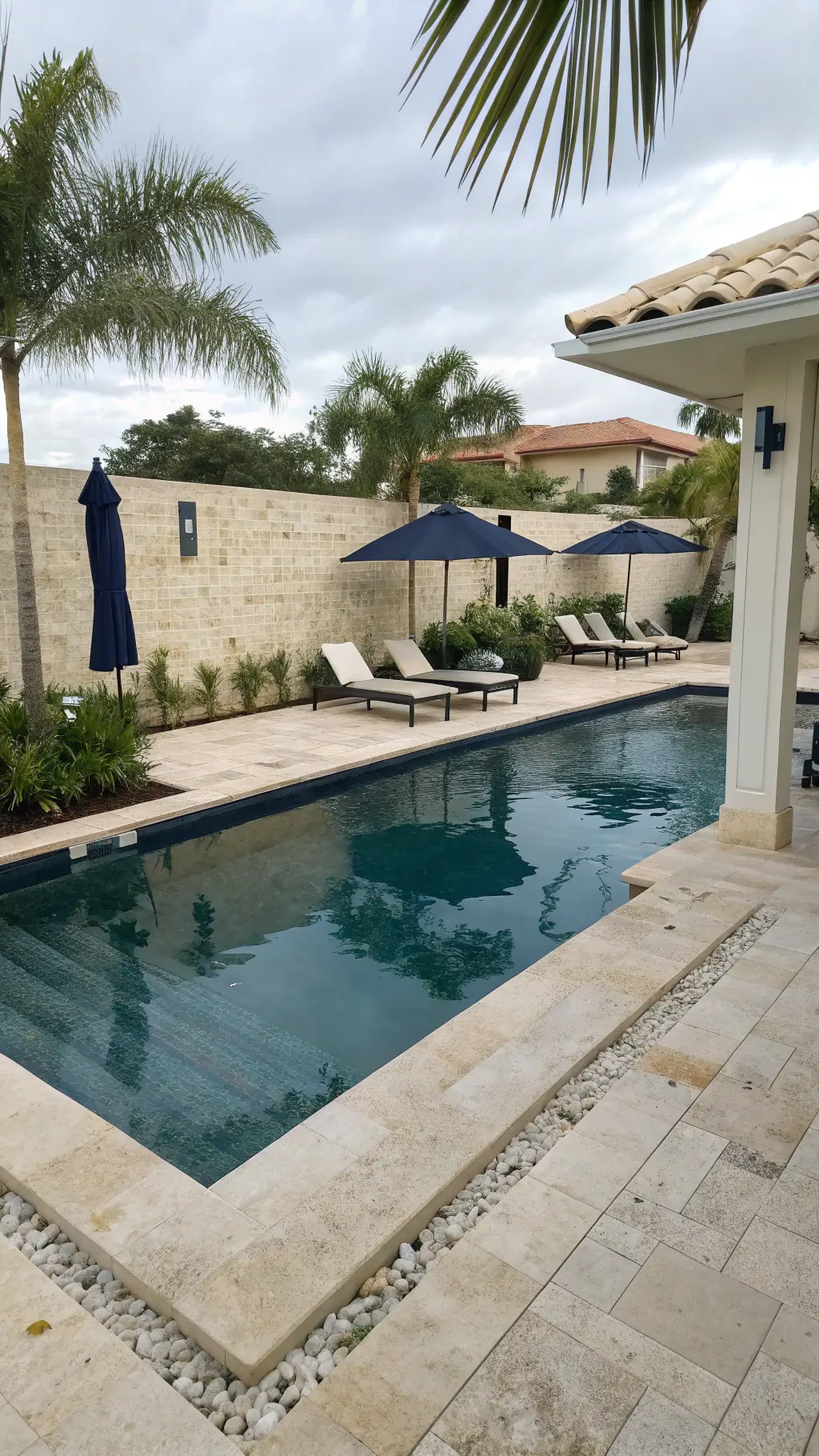 Luxurious pool with Baja steps, ivory travertine decking, navy umbrellas, white mesh chaise lounges, and potted palms providing shade