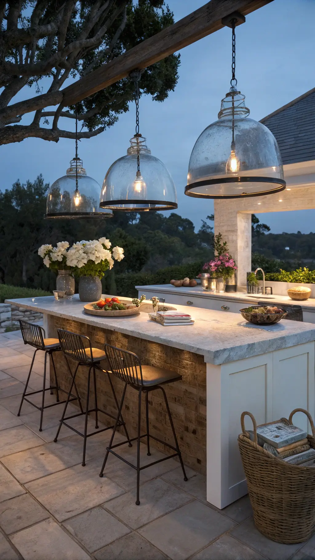 vintage-inspired kitchen island with marble top, metal stools, fresh flowers, cookbooks, baskets, glass dome pendant lights during blue hour